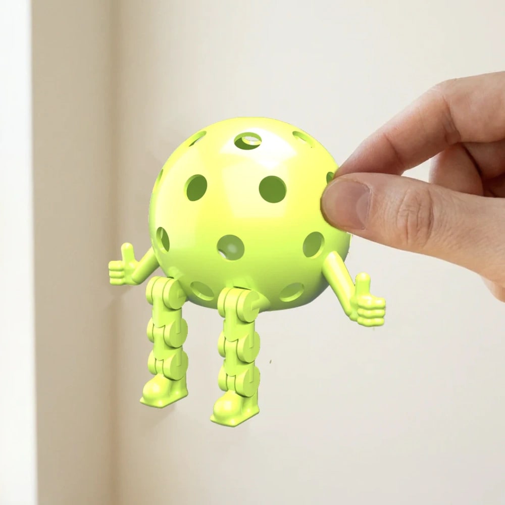 A hand holding a green Pickleball Dinky by the ball, arms and legs hanging free